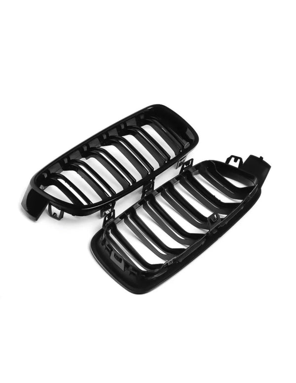 Two glossy black car grilles lie on a white background, featuring vertical slats and curved contours. The design suggests an automotive part, likely for a front bumper.