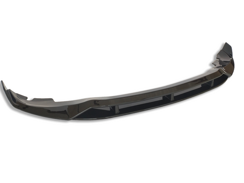 A glossy black car bumper lip sits isolated against a white background, showcasing its curved aerodynamic design and reflective surface.