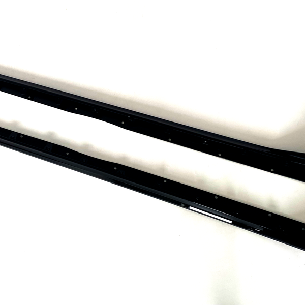 Two elongated black metal car side skirts lie parallel on a plain white surface, featuring multiple mounting holes along their length and slight contours for aerodynamic enhancement.