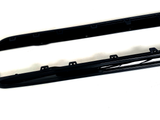 Two black car side skirts are resting on a white surface, featuring several mounting brackets along their length for attachment.