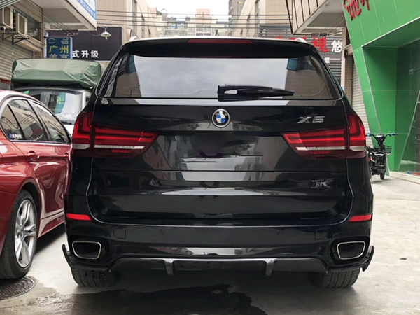 A black BMW X5 is parked beside a red car in an urban alley. The area is surrounded by buildings, with some signs in Chinese characters visible in the background.