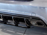 A car's rear bumper features dual exhausts and a black diffuser. The scene is indoors, with the vehicle parked on a glossy tiled floor.