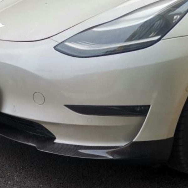 A white car with carbon fiber accents is parked on an asphalt surface. The license plate reads "CARBON ACCENTS."