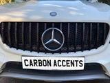 A car grille displays a prominent emblem and black vertical slats, situated on a white vehicle. The license plate reads 