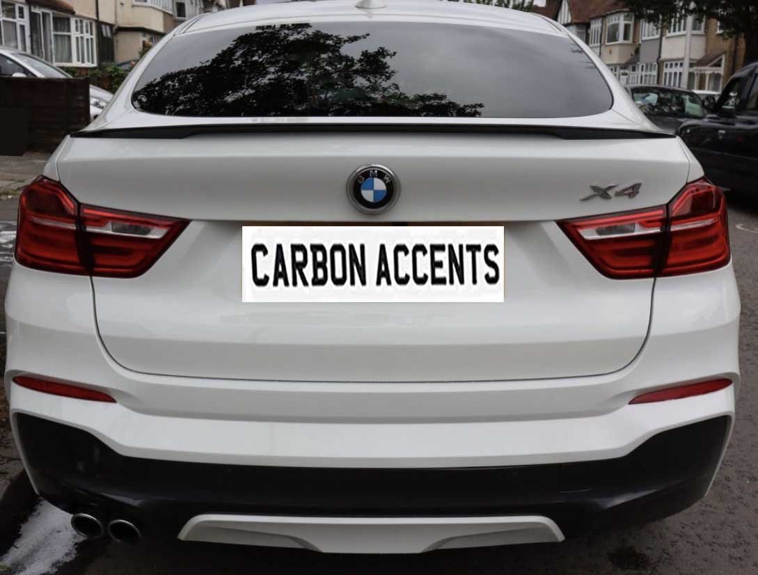 A white BMW X4 is parked on a residential street. The license plate reads "CARBON ACCENTS." Surrounding are houses and parked cars.