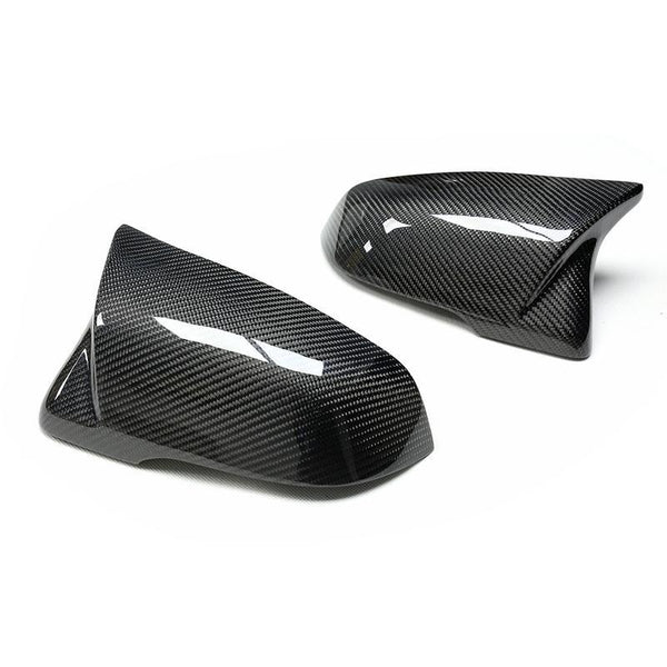 Two glossy, dark carbon fiber side mirror covers, positioned on a plain white background, showcasing their sleek, aerodynamic design and intricate pattern.