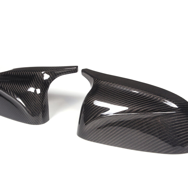 Two carbon fiber car mirror covers sit side by side on a plain white background, showcasing a glossy, reflective surface with a distinctive weave pattern.