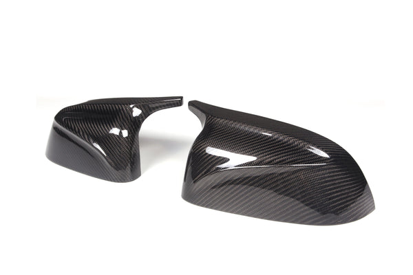 Two carbon fiber car mirror covers sit side by side on a plain white background, showcasing a glossy, reflective surface with a distinctive weave pattern.