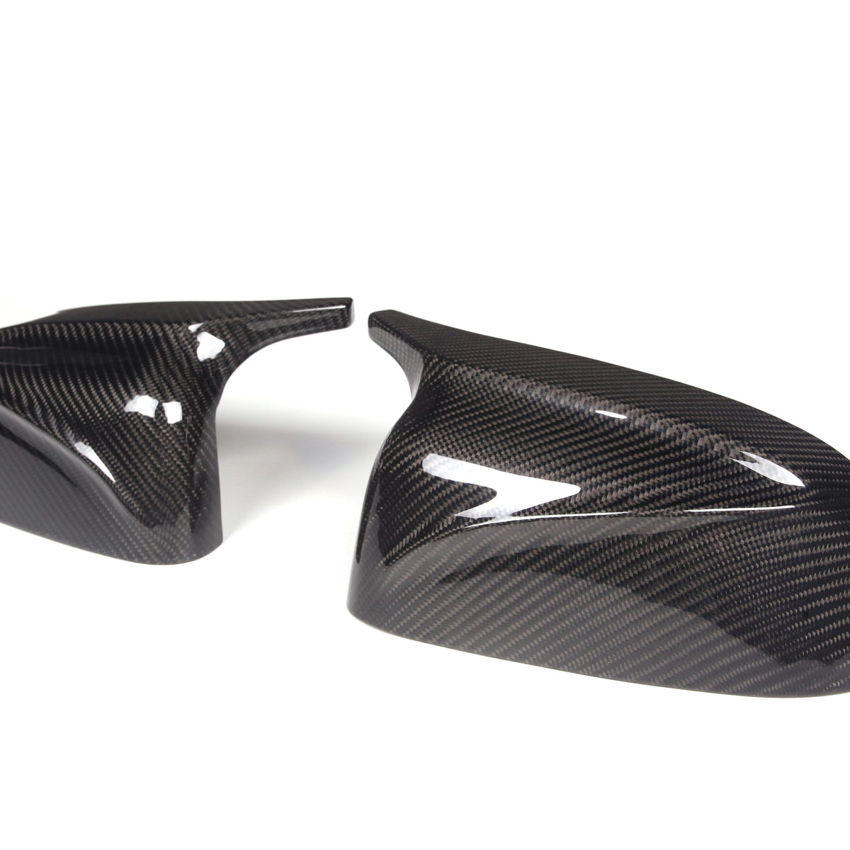 Two carbon fiber side mirror caps, resting on a white background, display a glossy, textured surface with reflective highlights, suggesting a sleek automotive accessory design.