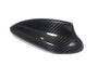 A carbon fiber car mirror cover, featuring a glossy, black textured surface, rests against a plain white background, highlighting its sleek design and curved aerodynamic shape.