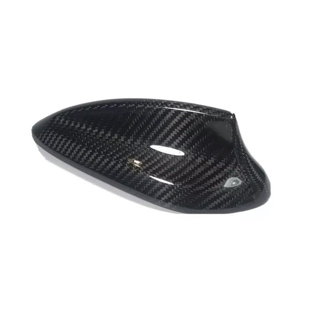 A carbon fiber car mirror cover, featuring a glossy, black textured surface, rests against a plain white background, highlighting its sleek design and curved aerodynamic shape.