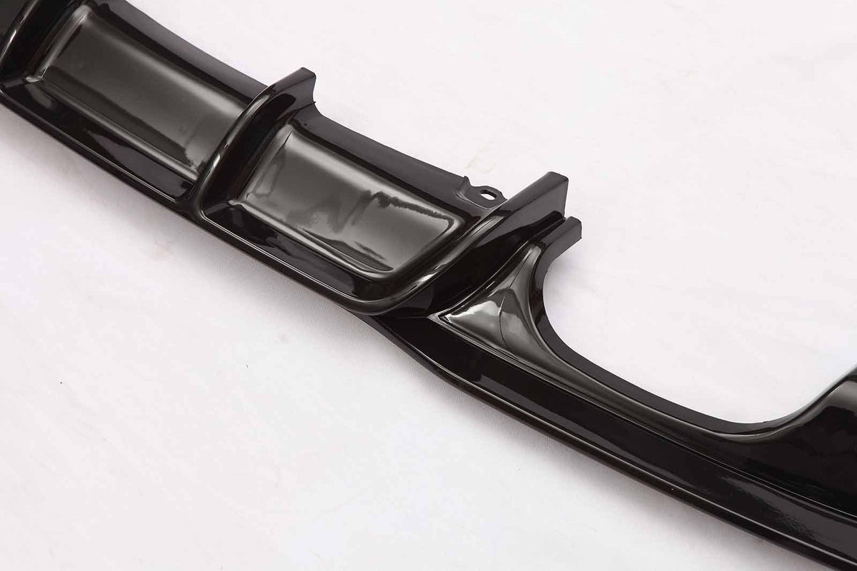 A shiny black car spoiler lies on a white background, displaying its sleek, aerodynamic fins and curves designed to reduce drag and enhance vehicle performance.