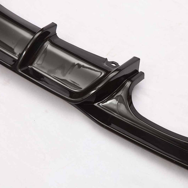 A shiny black car spoiler lies on a white background, displaying its sleek, aerodynamic fins and curves designed to reduce drag and enhance vehicle performance.