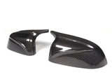 Two carbon fiber mirror covers, glossy with a black and gray weave pattern, are positioned against a plain white background. They exhibit a sleek, aerodynamic design.