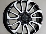 A black and white car wheel rim with a multi-spoke design is upright on a plain surface, set against a neutral background.