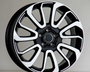 A black and white car wheel rim with a multi-spoke design is upright on a plain surface, set against a neutral background.
