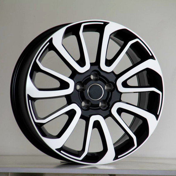 A black and white car wheel rim with a multi-spoke design is upright on a plain surface, set against a neutral background.
