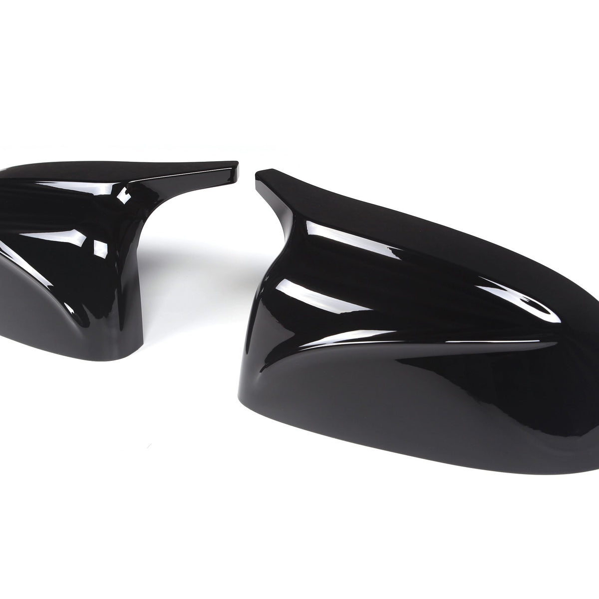 Two glossy black car mirror covers are lying on a plain white background. The covers have sleek aerodynamic designs, reflecting light prominently on their curved surfaces.