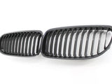 Two black car grille inserts with vertical slats lie side by side on a white background, resembling classic automotive front grille designs.