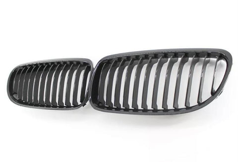 Two black car grille inserts with vertical slats lie side by side on a white background, resembling classic automotive front grille designs.