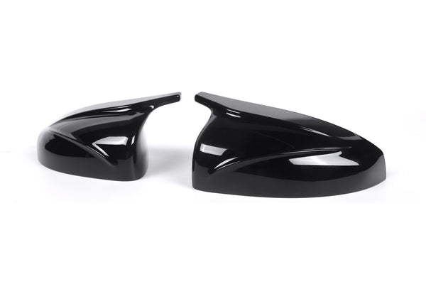 Two glossy black car mirror covers rest side by side, featuring sleek aerodynamic designs, set against a plain white background.