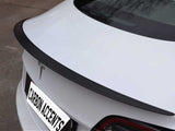 A white car features a sleek, black carbon fiber spoiler on its trunk. The car is parked outdoors, displaying a logo and a license plate reading 