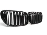 Two glossy black car grilles, featuring vertical slats, are positioned on a plain white background, angled slightly toward each other.