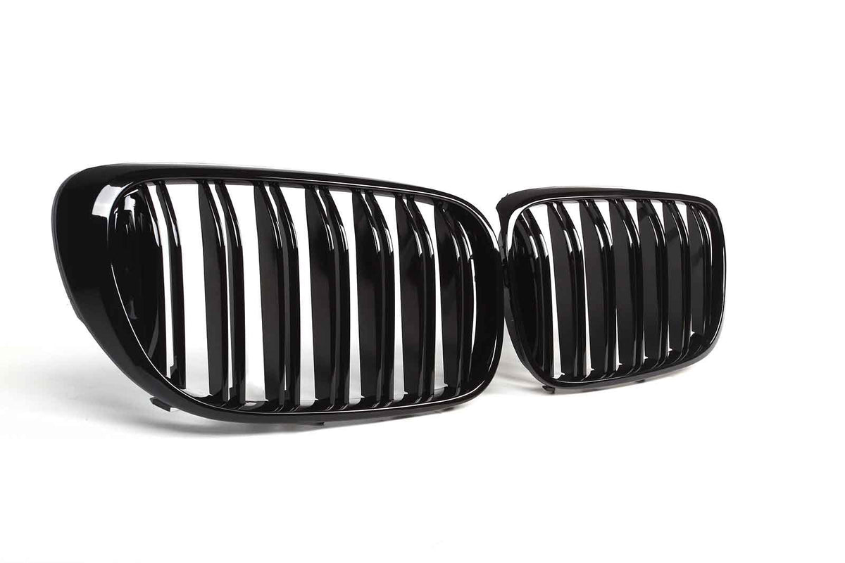 Two glossy black car grilles, featuring vertical slats, are positioned on a plain white background, angled slightly toward each other.
