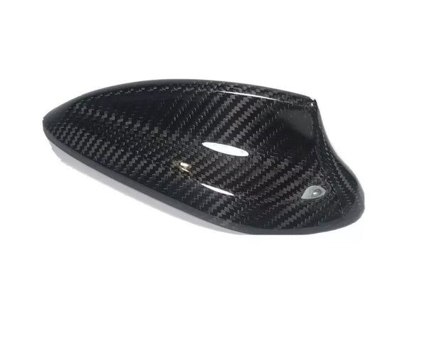 Carbon fiber car side mirror cover, sleek and glossy, resting on a plain white background. The cover exhibits a distinct woven pattern and aerodynamic design, emphasizing high-performance aesthetics.