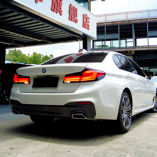 A white BMW with illuminated rear lights is parked under a building with Chinese signage, surrounded by other parked cars on a sunny day.