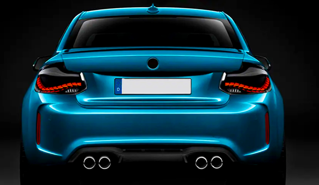 A sleek blue sports car is shown from the rear, featuring illuminated taillights and dual exhausts, set against a dark background. The license plate reads "D."