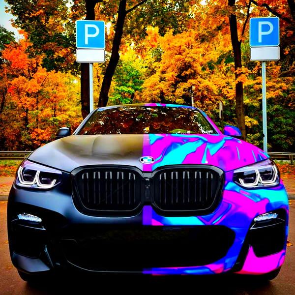 A car with one side in matte black and the other in vibrant purple and blue stands parked in front of two "P" parking signs. Autumn trees surround the area.