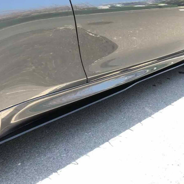A sleek, dark-colored car is parked on a sunlit street, showcasing its shiny surface and stylish, multi-spoke alloy wheels, with a reflection visible on the vehicle’s side panel.