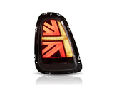 The object is a car taillight with a glowing red and amber graphic resembling a Union Jack. It's isolated against a plain white background, highlighting its distinctive design.
