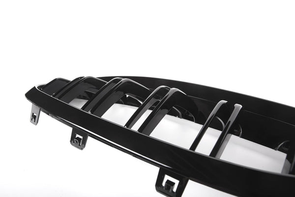 A glossy black car grille with vertical slats rests against a bright white background, featuring attachment clips at the bottom edge.