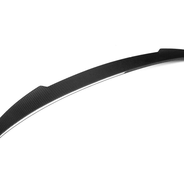 A curved, carbon-fiber car spoiler is shown in close-up, lying flat against a plain white background. It has a sleek, aerodynamic design with a textured surface.