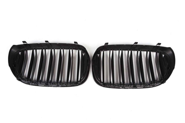 Two black car grille inserts rest on a white background, featuring vertical slats and curved edges, designed to fit the front of a vehicle.