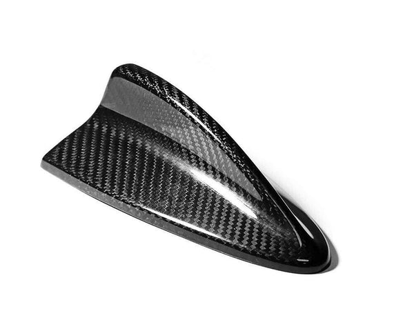 A black carbon fiber shark fin-shaped antenna is resting on a plain white background, highlighting its sleek, glossy texture and aerodynamic design.