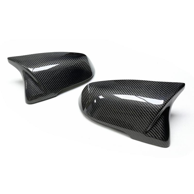 Carbon fiber mirror caps rest side by side on a white surface, displaying their glossy, textured design typically used for automotive exterior upgrades.