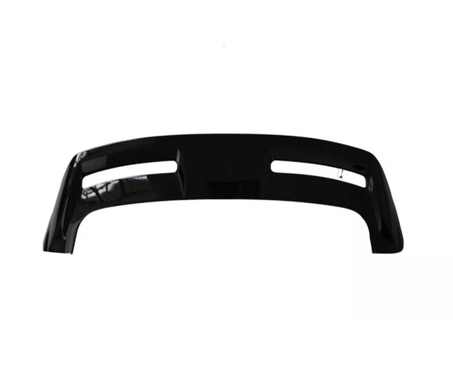 A black automotive bumper with two elongated cutouts lies on a plain, white background, showcasing its smooth surface and contoured design.