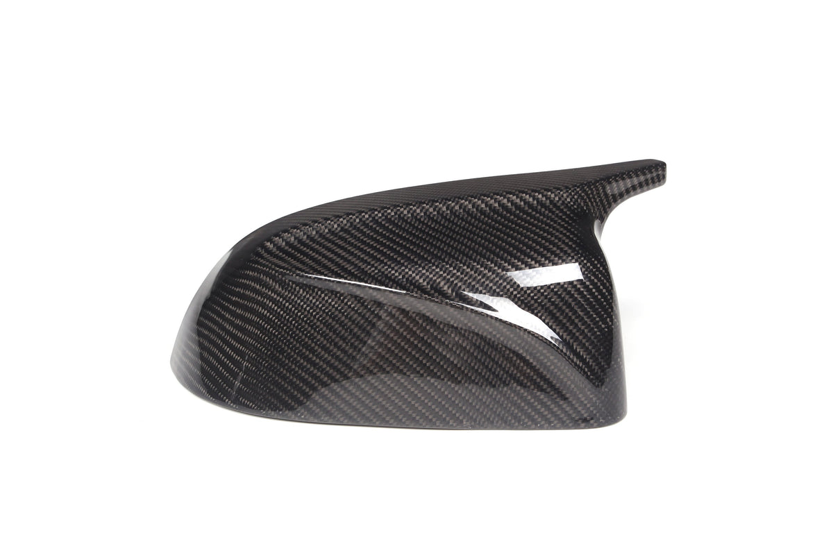 A sleek carbon fiber car mirror cover, reflecting light, sits against a plain white background, highlighting its glossy, textured surface and aerodynamic design.