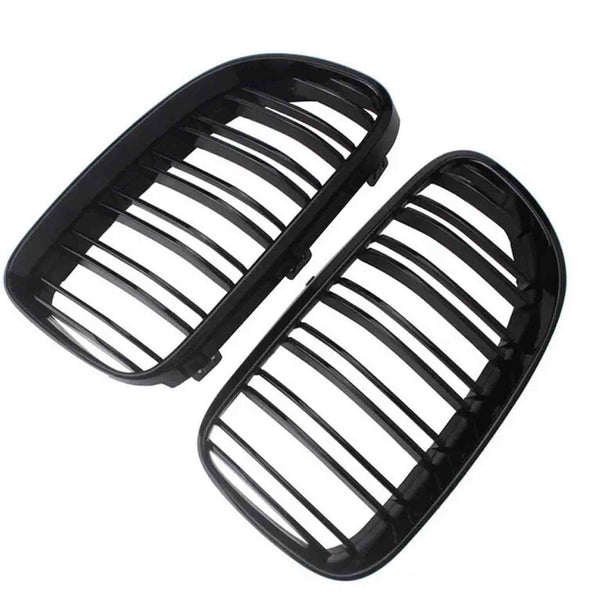 Two black car grille inserts, featuring vertical slats, lie angled against a white background. They are separated, showing both the front and back view of each grille.