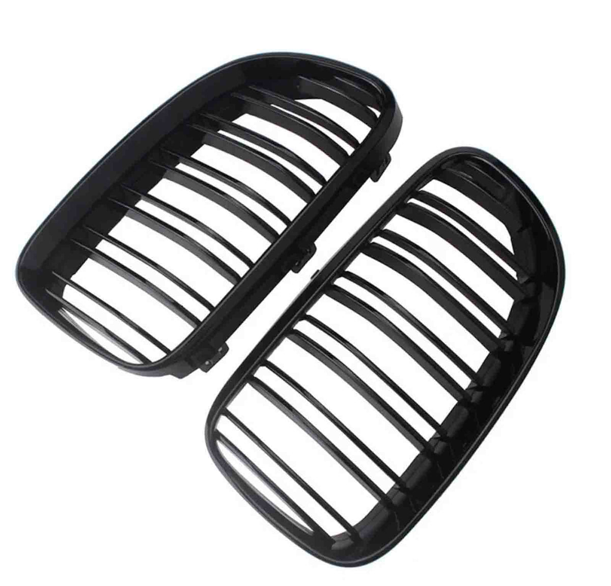 Two black car grille inserts, featuring vertical slats, lie angled against a white background. They are separated, showing both the front and back view of each grille.