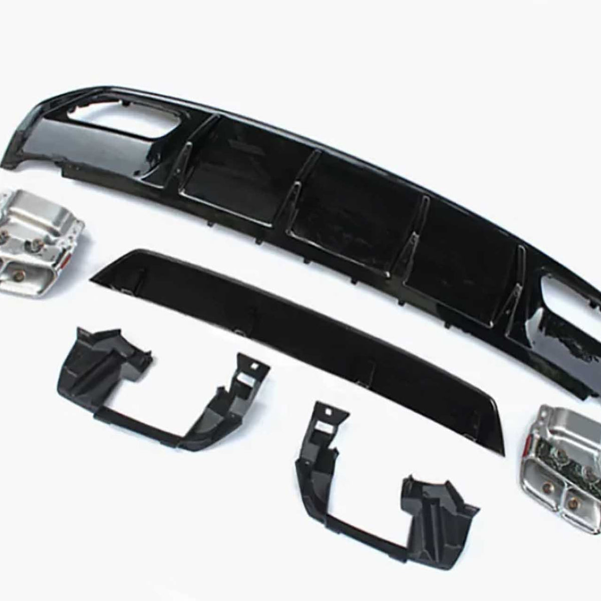 Car bumper components lie on a plain white surface, including black plastic and metallic parts arranged separately, showcasing a disassembled view typical for repairs or upgrades.