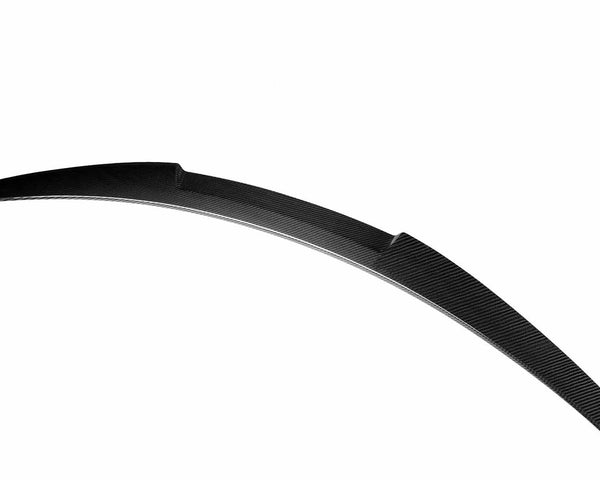 Curved carbon fiber component, likely a car spoiler, positioned diagonally against a white background. The textured pattern of the material is distinctly visible.