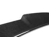 A glossy, black carbon fiber panel, angled slightly, sits under bright lighting, showcasing its textured weave pattern against a plain white background.