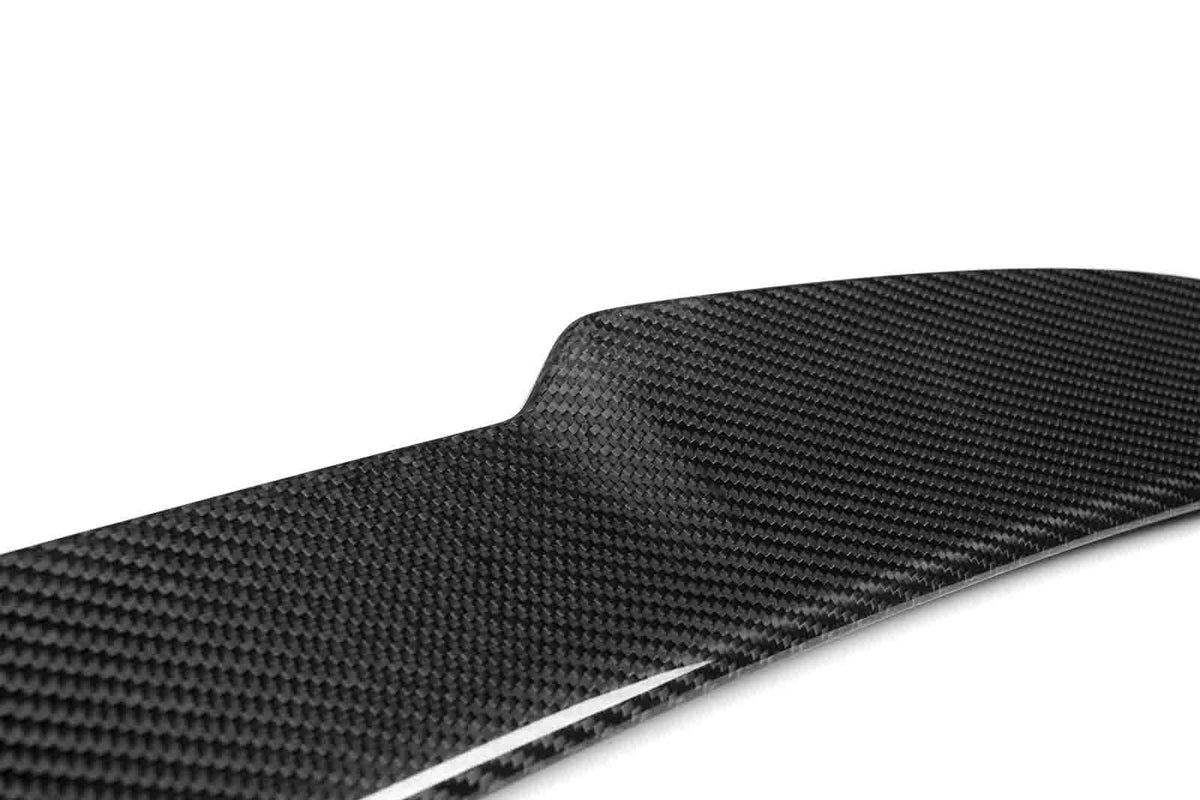 A glossy, black carbon fiber panel, angled slightly, sits under bright lighting, showcasing its textured weave pattern against a plain white background.