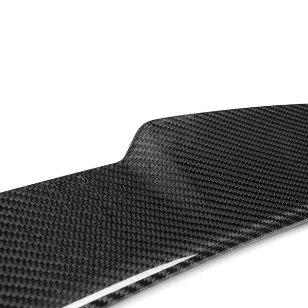 A glossy, black carbon fiber panel, angled slightly, sits under bright lighting, showcasing its textured weave pattern against a plain white background.