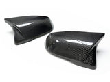 Two carbon fiber car side mirror covers are placed on a white surface, showcasing a glossy finish with fine diagonal patterning.