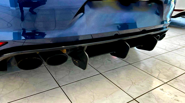 Four black exhaust pipes are protruding from the rear of a blue car, positioned over glossy tiled flooring in an indoor showroom setting.